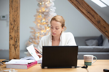 Image showing Young female entrepreneur wearing cosy warm bathrobe working remotly from home in winter Christmas time during 2020 corona virus pandemic. Work from home, selter in place, concept.