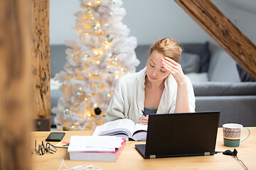 Image showing Young female entrepreneur wearing cosy warm bathrobe working remotly from home in winter Christmas time during 2020 corona virus pandemic. Work from home, selter in place, concept.