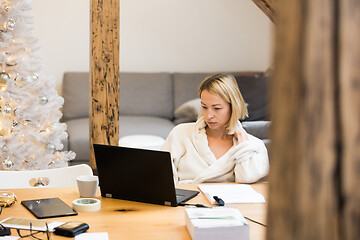 Image showing Young female entrepreneur wearing cosy warm bathrobe working remotly from home in winter Christmas time during 2020 corona virus pandemic. Work from home, selter in place, concept.