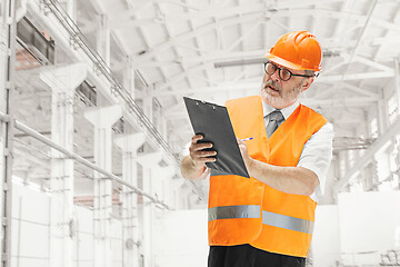 Image showing Professional senior builder in orange helmet against industrial background