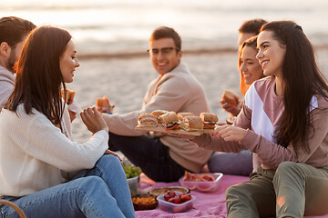 Image showing happy friends eating sandwiches at picnic on beach