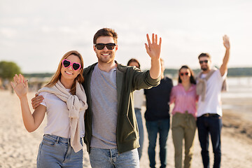 Image showing happy couple with friends waving hands on beach