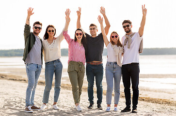 Image showing happy friends waving hands on beach in summer