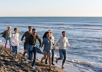 Image showing Group of friends running on beach during autumn day