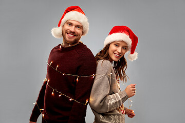 Image showing happy couple in christmas sweaters and santa hats