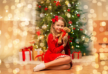 Image showing girl in red dress hugging teddy bear at home