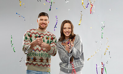 Image showing couple in christmas sweaters popping party poppers