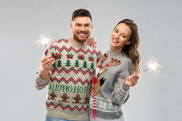 Image showing happy couple in christmas sweaters with sparklers