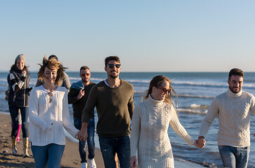 Image showing Group of friends running on beach during autumn day