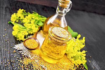 Image showing Oil mustard in jar and decanter with flower on dark board