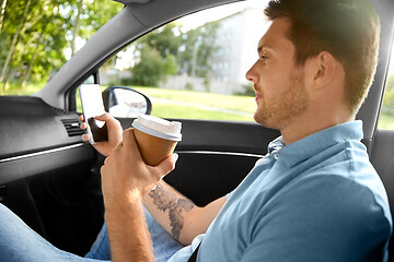 Image showing passenger drinking coffee using smartphone in car