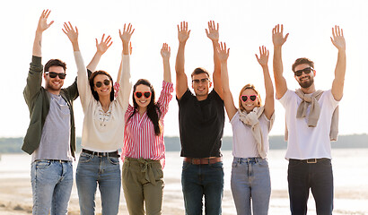 Image showing happy friends waving hands on beach in summer