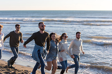 Image showing Group of friends running on beach during autumn day