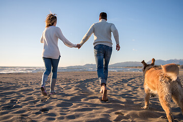 Image showing couple with dog having fun on beach on autmun day