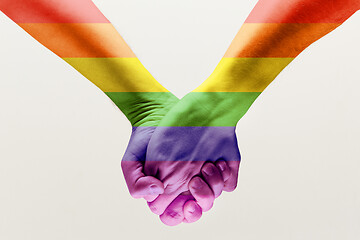 Image showing  loseup of a gay couple holding hands, patterned as the rainbow flag