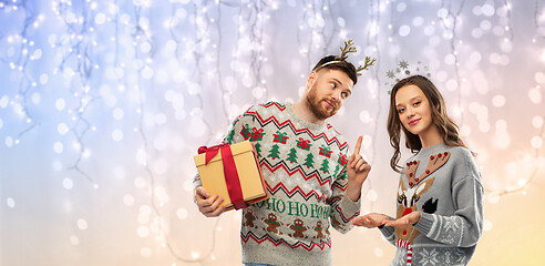 Image showing happy couple in ugly sweaters with christmas gift