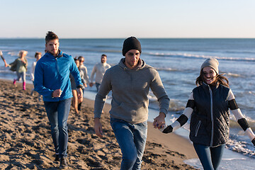 Image showing Group of friends running on beach during autumn day