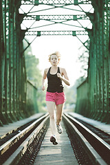 Image showing Athlete running on railaway bridge training for marathon and fitness. Healthy sporty caucasian woman exercising in urban environment before going to work. Active urban lifestyle