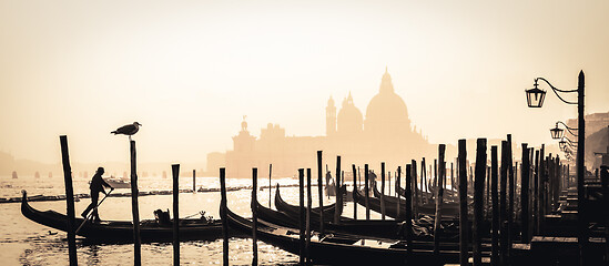 Image showing Romantic Italian city of Venice, a World Heritage Site: traditional Venetian wooden boats, gondolier and Roman Catholic church Basilica di Santa Maria della Salute in the misty background