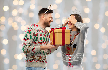 Image showing happy couple in ugly sweaters with christmas gift