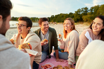 Image showing happy friends eating sandwiches at picnic on beach