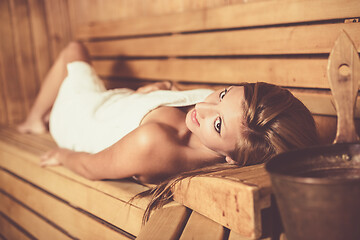 Image showing Lady relaxing in traditional wooden Finnish sauna.