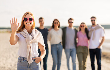 Image showing woman with friends on beach in summer waving hand