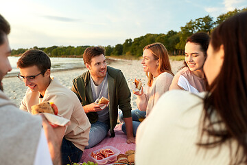 Image showing happy friends eating sandwiches at picnic on beach