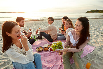 Image showing happy friends eating sandwiches at picnic on beach