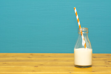 Image showing Glass milk bottle half full with a retro paper straw
