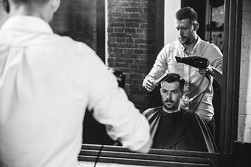 Image showing Young handsome barber making haircut for attractive man in barbershop