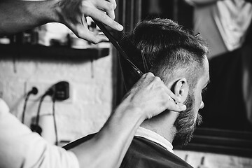 Image showing Young handsome barber making haircut for attractive man in barbershop