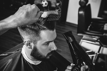 Image showing Young handsome barber making haircut for attractive man in barbershop