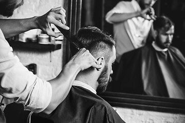 Image showing Young handsome barber making haircut for attractive man in barbershop