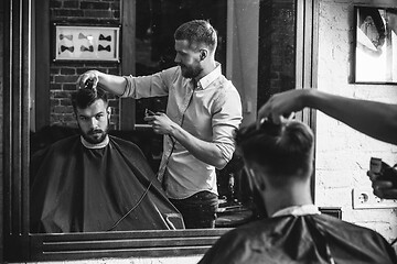 Image showing Young handsome barber making haircut for attractive man in barbershop