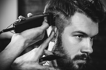 Image showing Young handsome barber making haircut for attractive man in barbershop