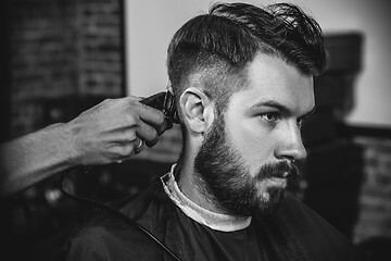 Image showing Young handsome barber making haircut for attractive man in barbershop