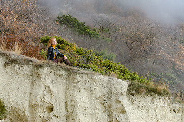 Image showing A girl sits on a hillock in the mountains and enjoys a wonderful view