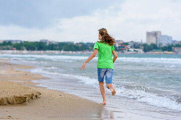 Image showing A girl happily runs along the sea coast, view from the back