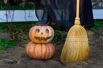 Image showing On a pumpkin with a drawn scary face is a witch\'s foot, next to a broom, close-up