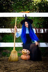 Image showing A girl in a witch costume sits on two pumpkins and holds a broom in her hands