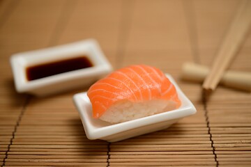 Image showing chopsticks, soy sauce and sushi with salmon on the mat