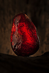 Image showing Beauty of natural raw amber. A piece of dark red semi transparent natural amber on piece of stoned wood.