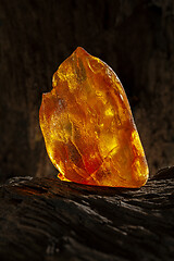 Image showing Beauty of natural raw amber. A piece of yellow opaque natural amber on large piece of dark stoned wood.