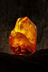 Image showing Beauty of natural raw amber. A piece of yellow opaque natural amber on large piece of dark stoned wood.