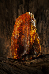 Image showing Beauty of natural raw amber. A piece of yellow opaque natural amber on large piece of dark stoned wood.