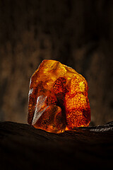 Image showing Beauty of natural raw amber. A piece of yellow and red semi transparent natural amber on piece of stoned wood.