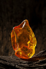 Image showing Beauty of natural raw amber. A piece of yellow opaque natural amber on large piece of dark stoned wood.