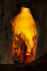 Image showing Beauty of natural raw amber. A piece of yellow opaque natural amber on large piece of dark stoned wood.