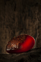 Image showing Beauty of natural raw amber. A piece of dark red semi transparent natural amber on piece of stoned wood.